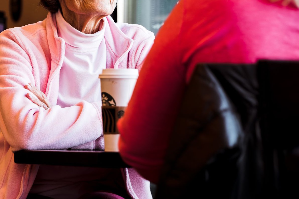 An adult daughter and her elderly mother talking warmly over cups of tea